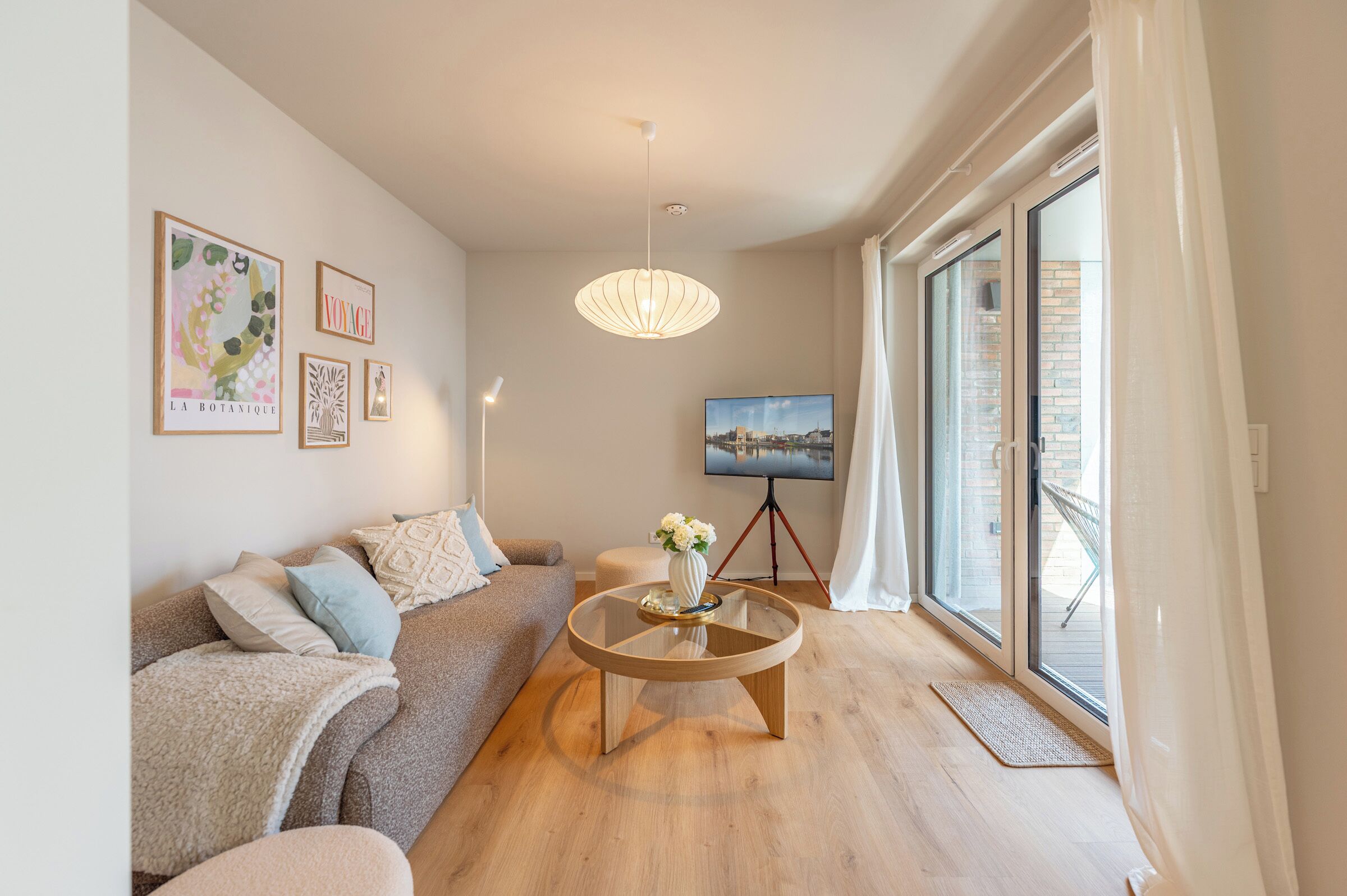 Un salon moderne avec un canapé, une table basse, un téléviseur et des œuvres d’art accrochées au mur.