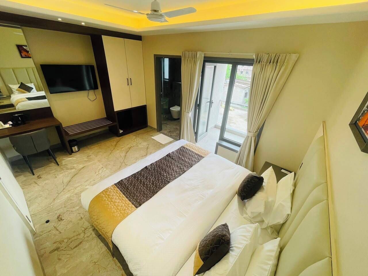 A hotel room with a bed, a desk, a television, and a sliding door to the balcony.