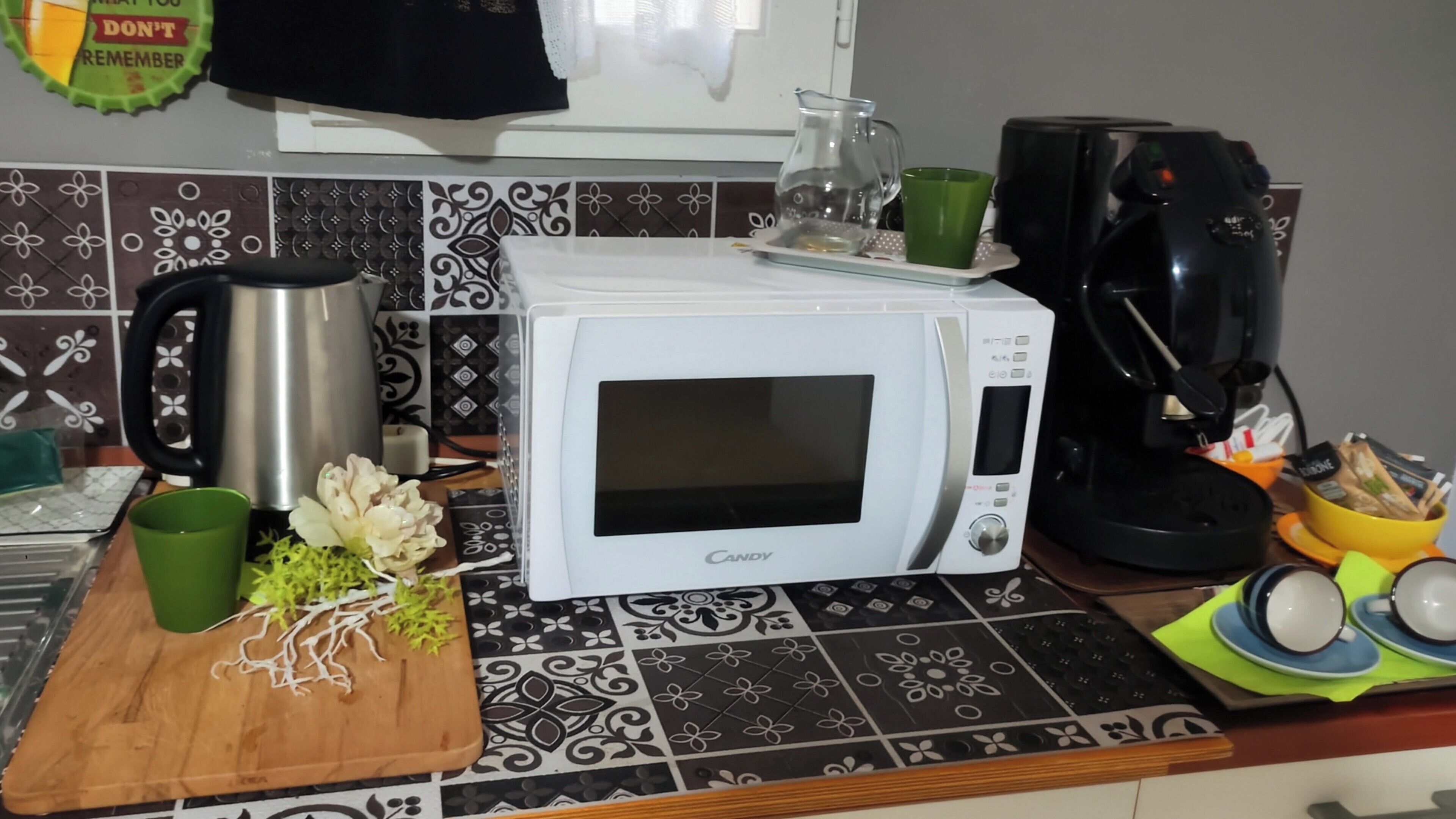 Una cocina con un microondas blanco, una cafetera y una tabla de cortar con verduras.