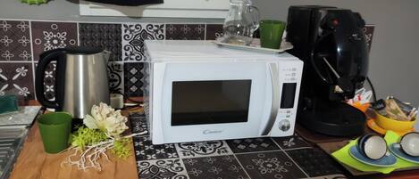 A kitchen with a white microwave, a coffee maker, and a cutting board with vegetables.