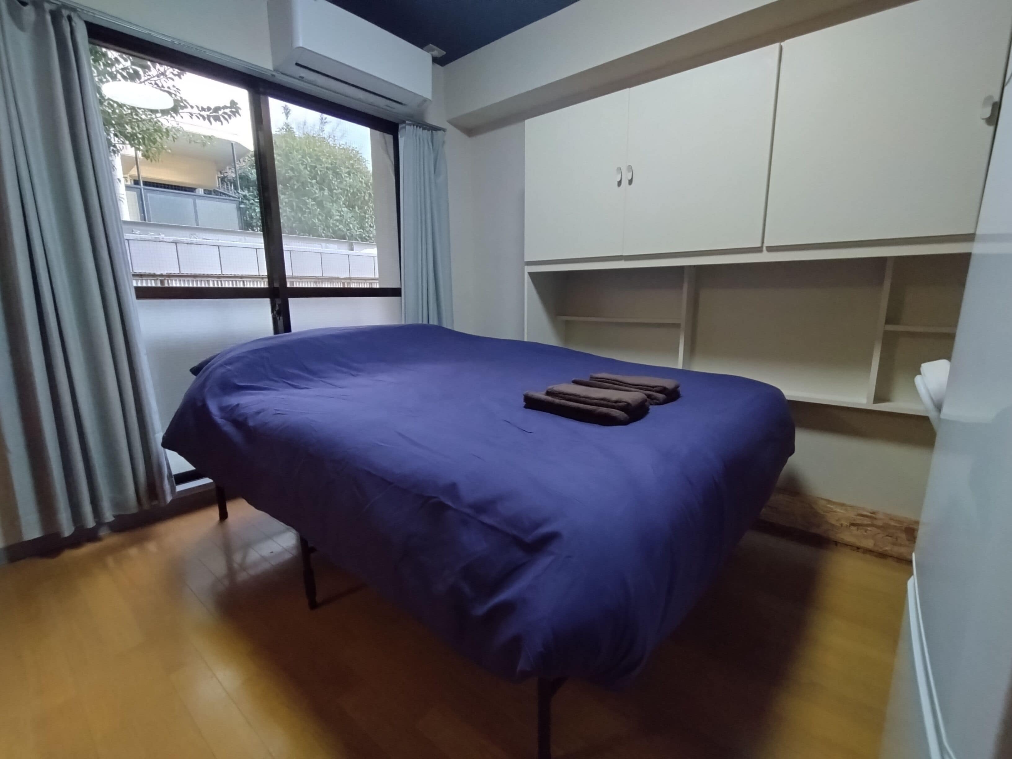 A room with a bed, a window with curtains, an air conditioning unit, and a built-in wardrobe.