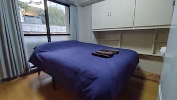 A room with a bed, a window with curtains, an air conditioning unit, and a built-in wardrobe.