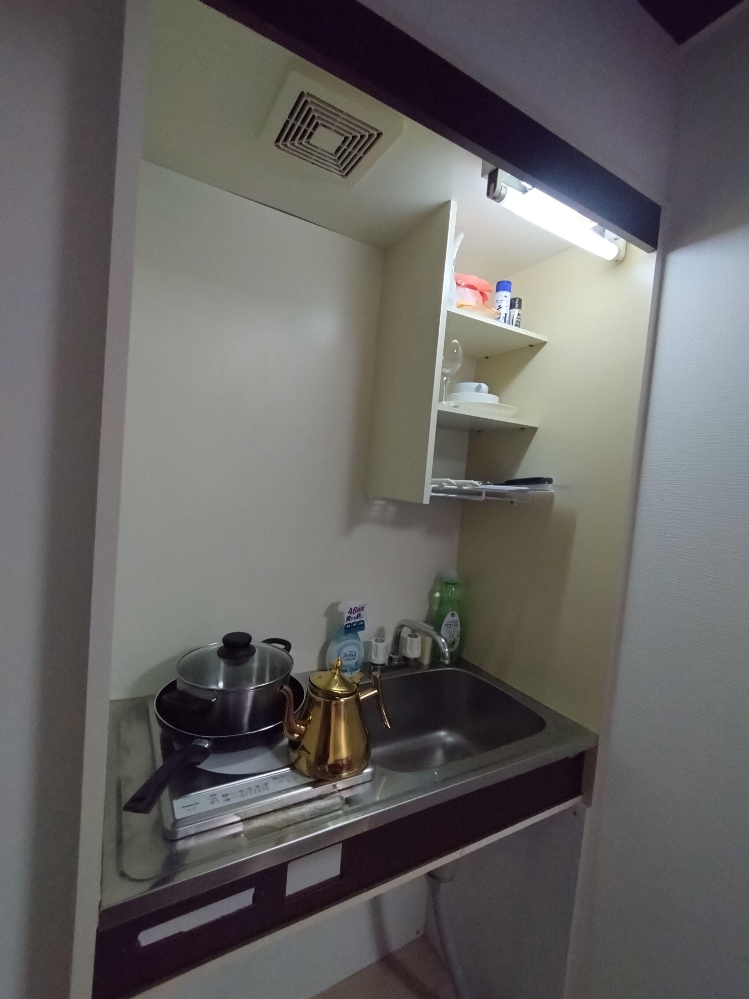 A compact kitchen with a sink, a stove, a kettle, and a mirror above the counter.