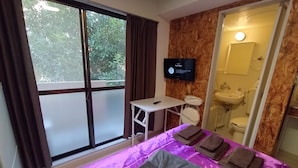 Habitación de hotel con cama, escritorio pequeño, televisor, baño con lavamanos e inodoro, y ventana con cortinas.