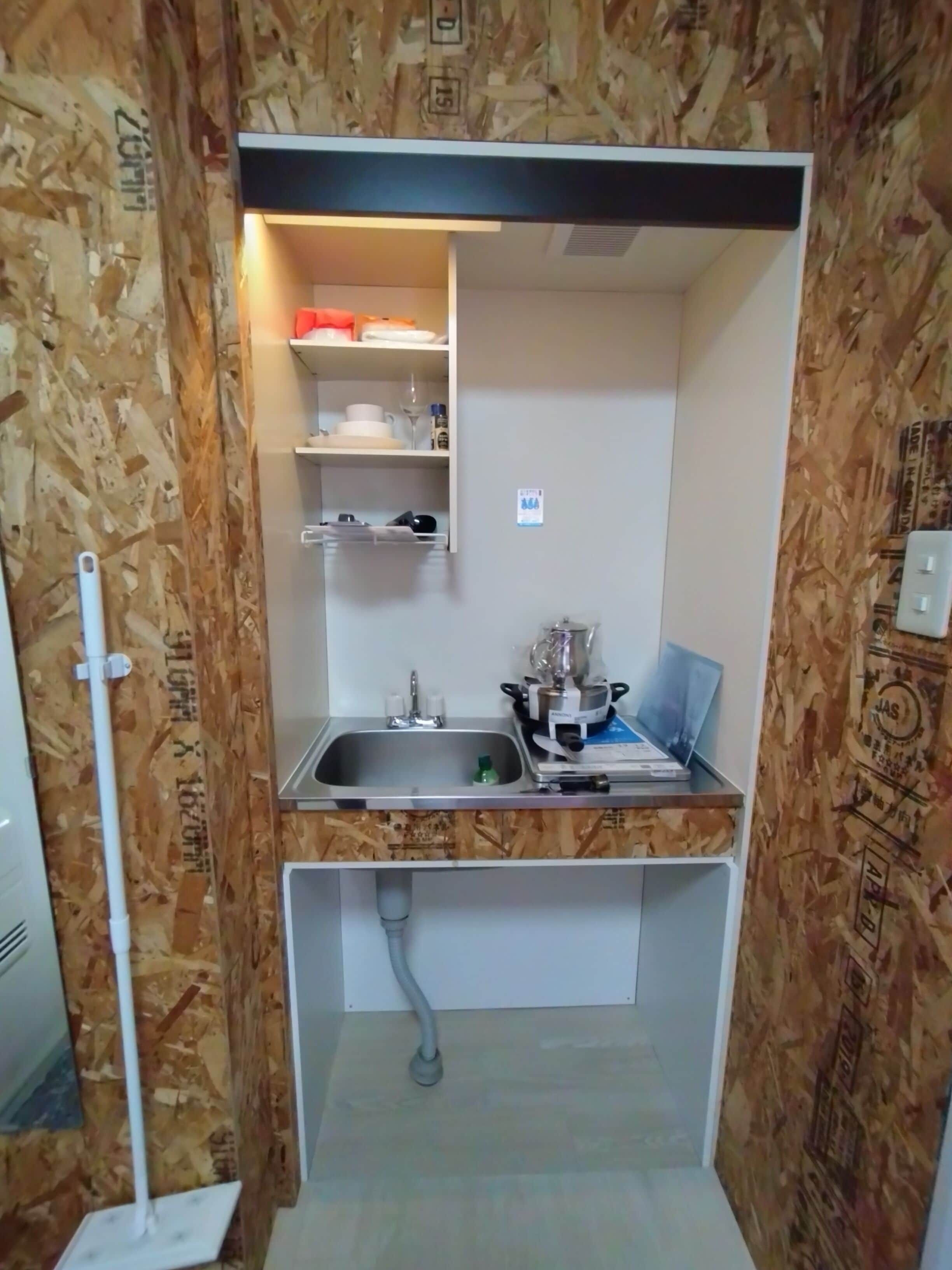 A compact kitchen with a built-in sink, a small countertop, and a shelf above the sink.