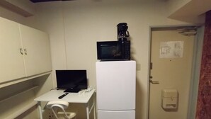 Una pequeña kitchenette con microondas, refrigerador, una laptop y una silla.