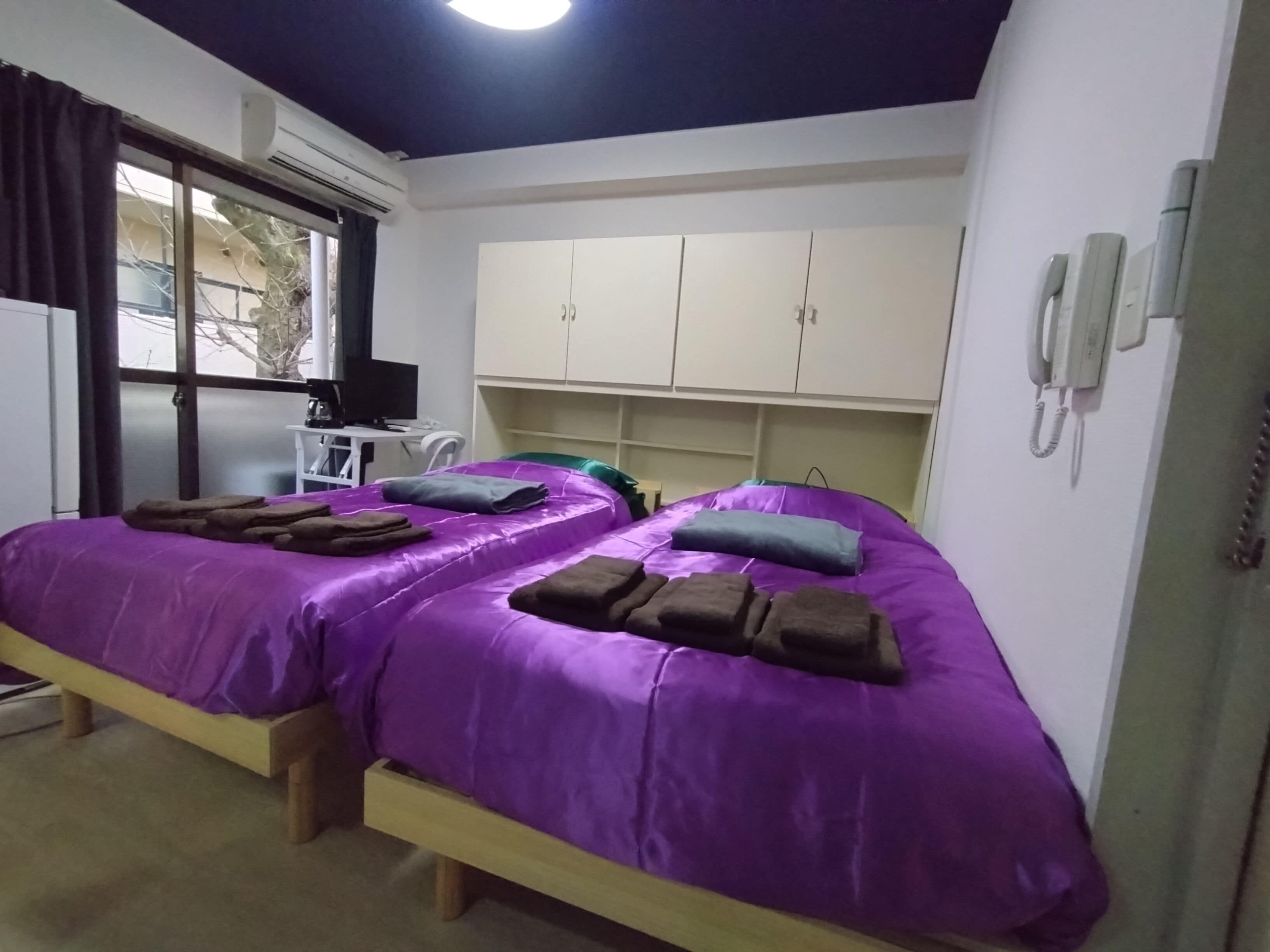 A room with two beds, a desk with a computer, and a window with curtains.