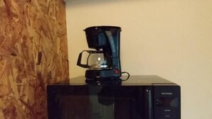 Un microondas con una cafetera encima, sobre una superficie blanca frente a una pared de madera.