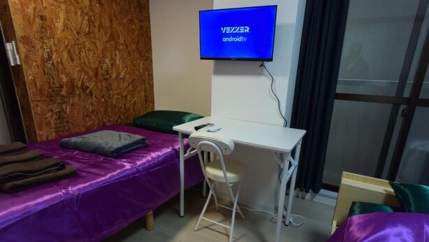 Una habitación con una cama, un escritorio y una silla. Hay un televisor colocado en la pared.