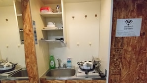 Cocina compacta con un lavamanos, estufa y encimera. Hay un cartel que indica que el apartamento tiene contraseña.