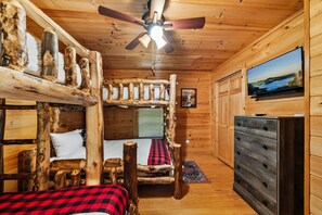 Ein Blockhaus-Interieur mit Etagenbett, Deckenventilator, Fernseher und Holzwänden.