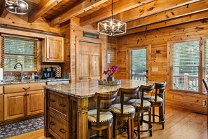A wooden cabin interior with a kitchen, bar area, and large windows. - Riverfront Cabin: Hot Tub, Sauna, Arcade & Views (Ellijay)
