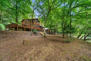 A cabin with a wooden deck and a staircase leading to a second level. - Riverfront Cabin: Hot Tub, Sauna, Arcade & Views (Ellijay)