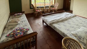 Une chambre avec deux lits simples, une chaise en bois, une petite table et une fenêtre avec des rideaux.