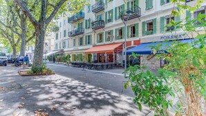 Eine Straße mit Außenbestuhlung, ein Restaurant namens 'Restaurant Indien' und ein Gebäude mit Balkonen und grünen Fensterläden.