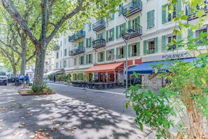 A street with outdoor seating, a restaurant named 'Restaurant Indien,' and a building with balconies and green shutters. - PIAZZA GRIMALDI AP4519 by Riviera Holiday Homes (Nice)