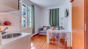 Eine kompakte Küche mit Spüle, ein Essbereich mit Tisch und Stühlen sowie ein Blick auf ein Gebäude durch ein Fenster.