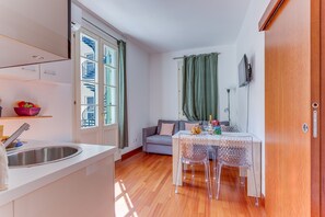 A compact kitchen with a sink, a dining area with a table and chairs, and a view of a building through a window. - PIAZZA GRIMALDI AP4519 by Riviera Holiday Homes (Nice)