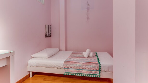 Ein kleines Schlafzimmer mit rosa Wänden, einem Einzelbett, Holzboden und einem Fenster.