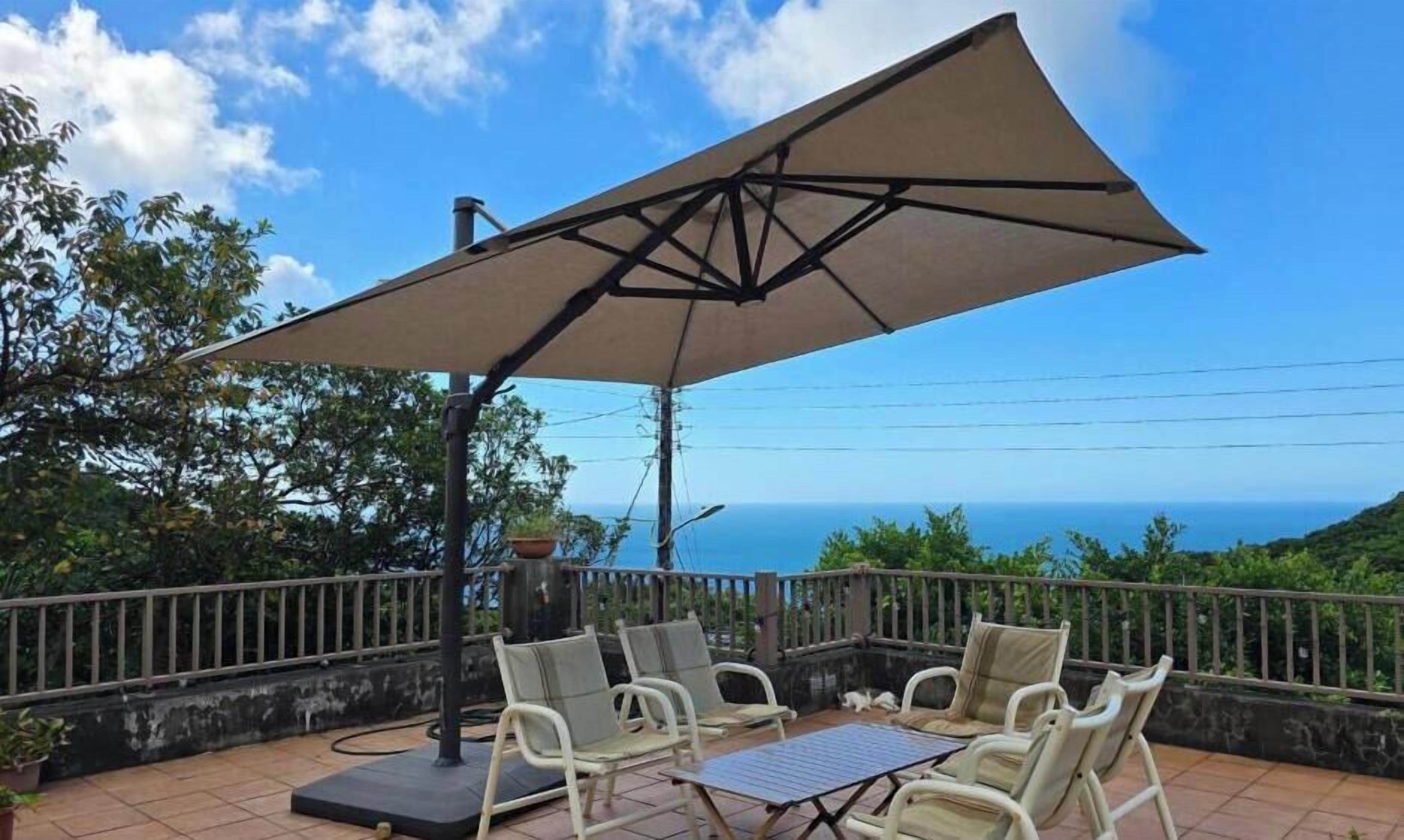 An outdoor seating area with a table and chairs, a large umbrella, and a view of the ocean.