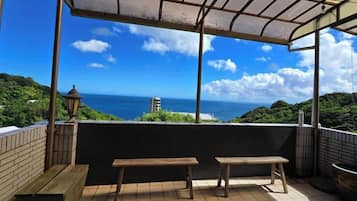 A covered outdoor seating area with a view of the ocean and greenery.