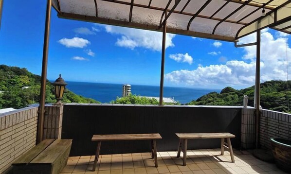 A covered outdoor seating area with a view of the ocean and greenery. - MiCasa Homestay (New Taipei City)