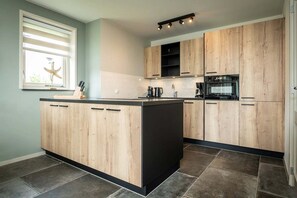 Eine moderne Küche mit Holzschränken, einer zentralen Kochinsel und einem Fenster mit Jalousien.