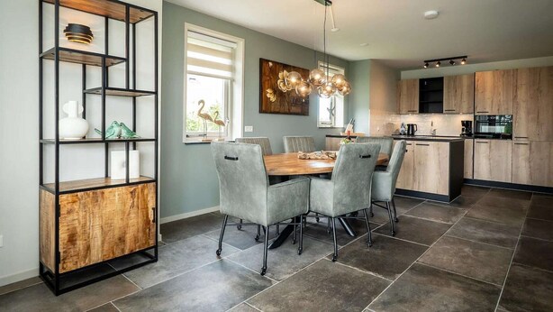 Une cuisine moderne avec un coin repas, comprenant une table à manger en bois, des chaises à revêtement gris et une étagère en métal noir.