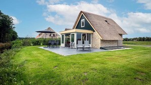 A house with a large patio area, a covered outdoor seating area, and a grassy yard.