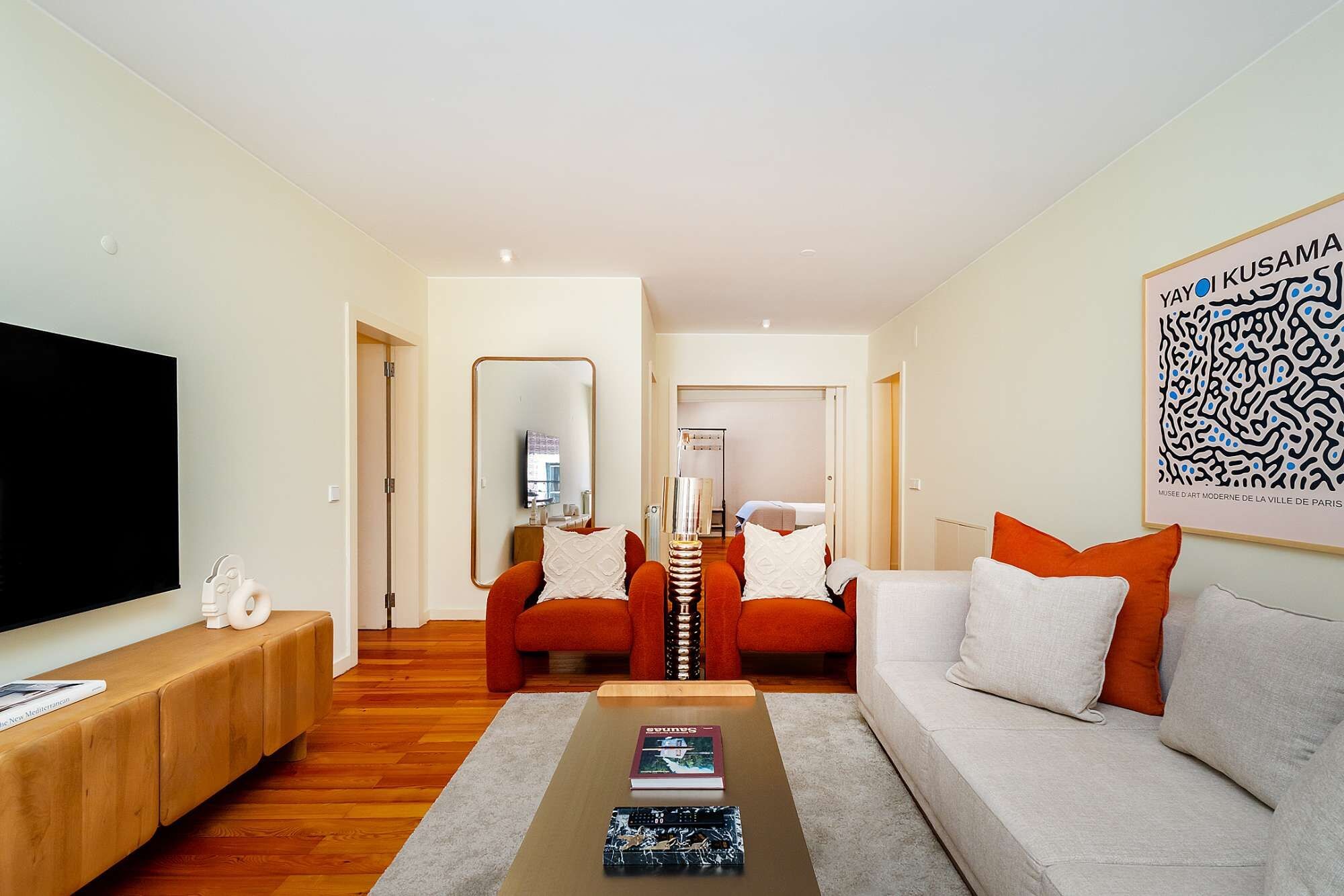 Ein modernes Wohnzimmer mit einer Couch, Sesseln, einem Couchtisch und einem Flachbildfernseher.