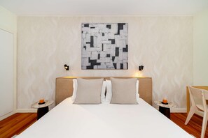 A hotel room with a large bed, two bedside tables with lamps, a wall-mounted abstract art piece, and a small round table with a chair. - Experience the Spirit of Historic Lisbon (Lisbon)