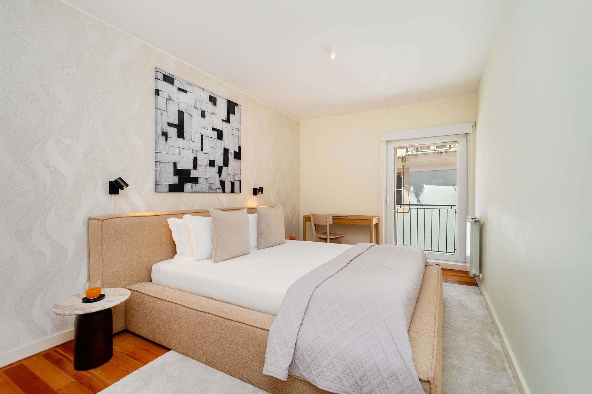 A bedroom with a bed, bedside tables, a desk, and a view of the outside.