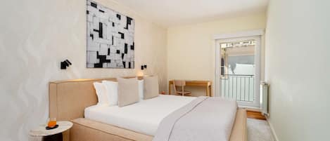 A bedroom with a bed, bedside tables, a desk, and a view of the outside.