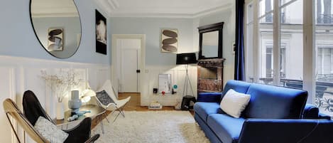 A living room with a blue sofa, a round mirror, and a white rug.