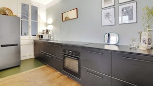 Una cocina moderna con refrigerador, horno, microondas y un lavamanos. Hay cuadros en la pared y un florero con flores en la encimera.