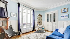 Una sala de estar con un sofá azul, una silla negra, un sillón blanco, una mesita redonda pequeña y un tapete blanco mullido.