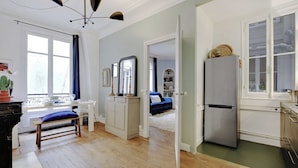 Una habitación con una mesa de comedor, sillas, un banco, un espejo, un armario, una cama, un refrigerador y una ventana.
