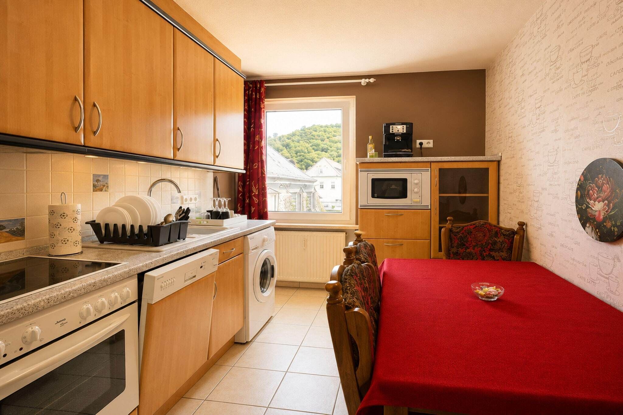 A compact kitchen with a washing machine, a microwave, and a dining area with a red tablecloth.