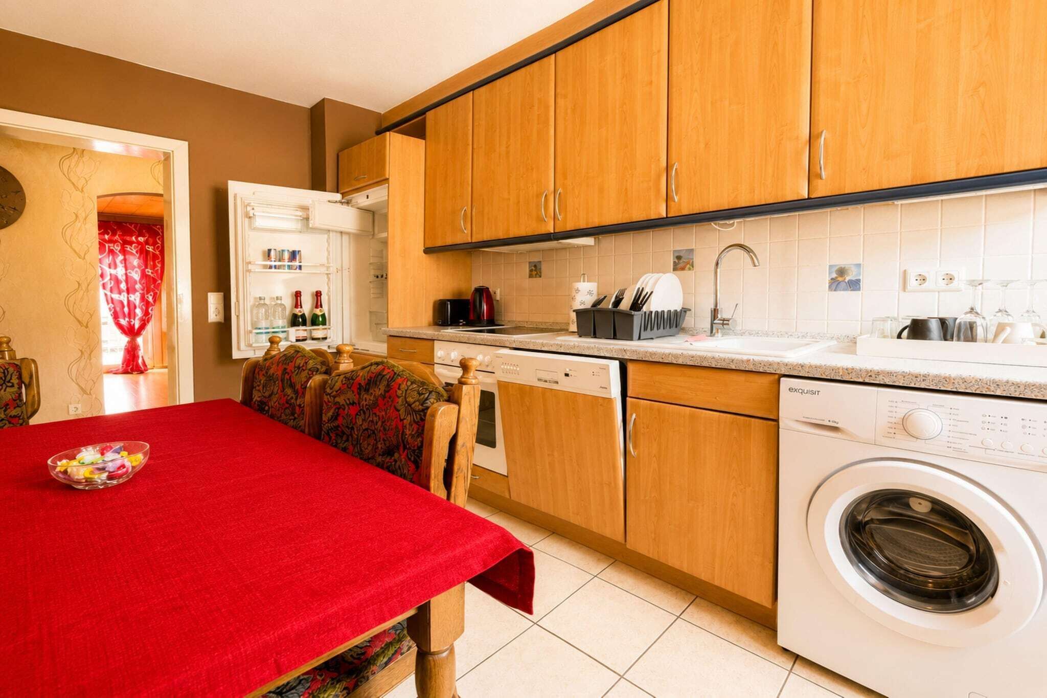 Una cucina funzionale con mobili in legno, lavatrice integrata e zona pranzo con tovaglia rossa.