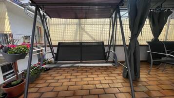 Ein überdachter Patio-Bereich mit einer Schaukel, Blumentöpfen und einem Stuhl.