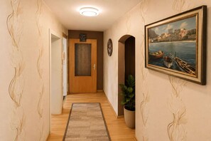 A hallway with a wooden door, a clock, a framed painting of a coastal scene, and a potted plant. - Taking a breather on the rooftops of Boppard (Boppard)