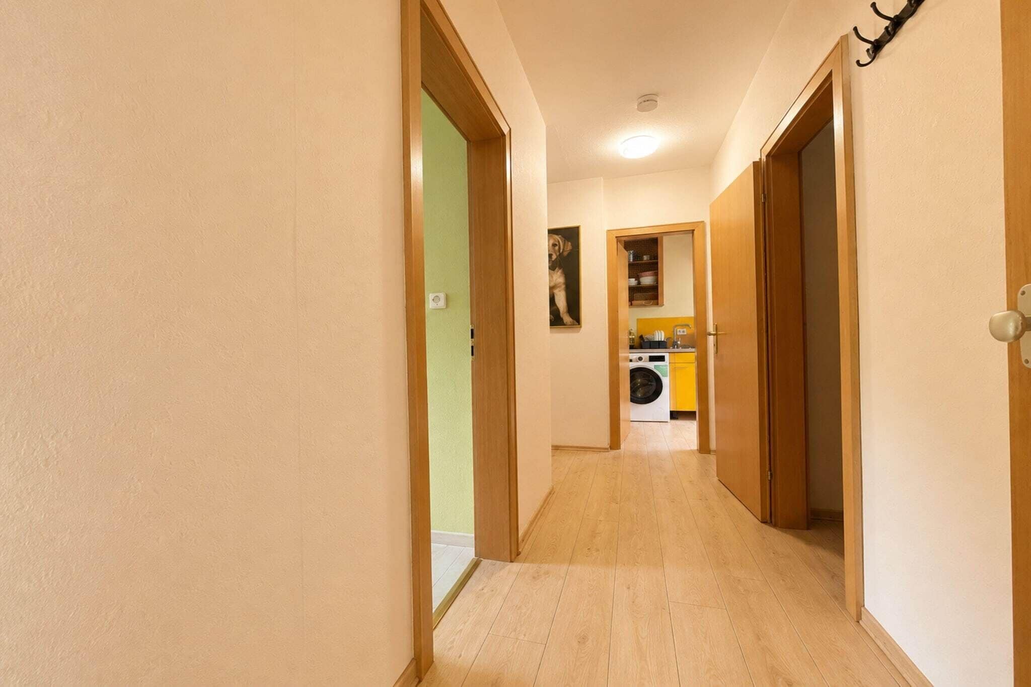 Un pasillo estrecho con suelo de madera que conduce a un área de lavandería con lavadora y lavabo.