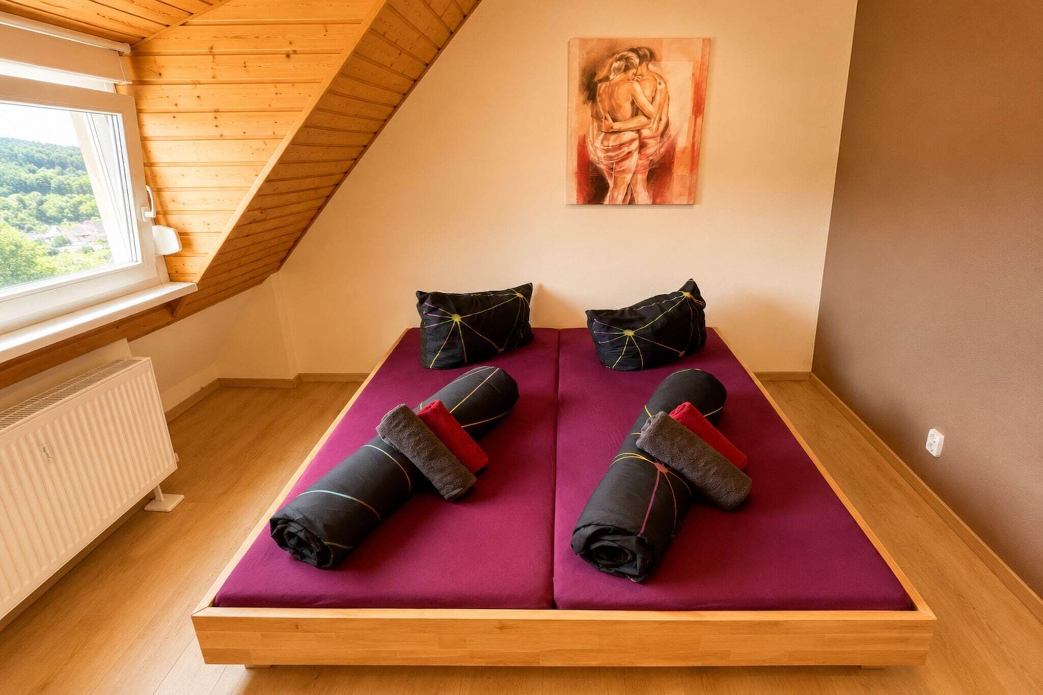 Una habitación con techo inclinado, una cama con colchón morado y un cuadro en la pared.