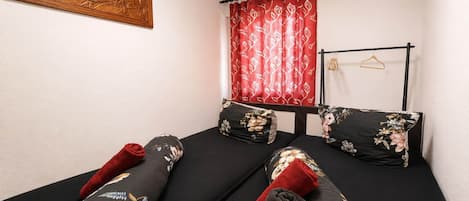 A room with a bed, a wooden wall art, a red curtain, and a black metal rack with hangers.