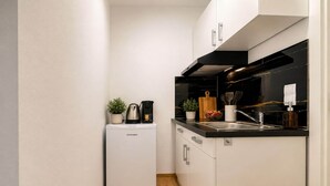 Una cocina compacta con armarios blancos, horno integrado, cafetera y lavabo.