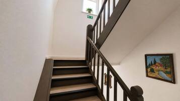 A staircase with wooden steps and dark railings, a small window with a plant, and a painting on the wall.