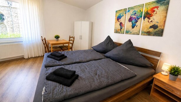 Un dormitorio con cama, escritorio, silla, armario y ventana con cortinas.