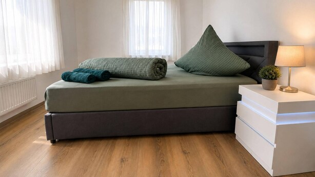 Une chambre à coucher moderne avec un lit, des oreillers, une table de chevet avec une lampe et une plante en pot.