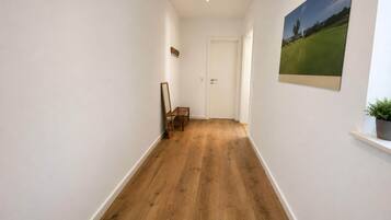 A hallway with wooden flooring, a door at the end, and a framed picture on the wall.