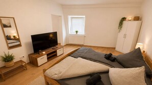 Een slaapkamer met een bed, televisie, raam, kast en spiegel.